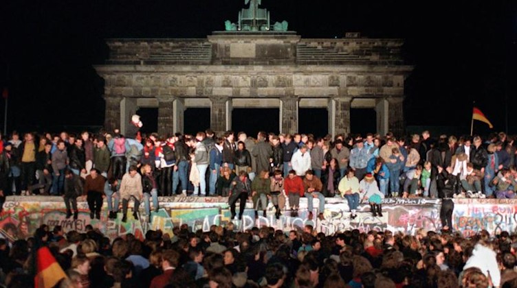 Jubelnde Menschen auf der Berliner Mauer am Brandenburger Tor. Foto: Wolfgang Kumm/Archivbild
