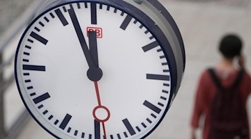 Eine Frau geht im Hauptbahnhof Dresden hinter einer Bahnhofsuhr auf einem Bahnsteig entlang. Foto: Sebastian Kahnert/Archivbild