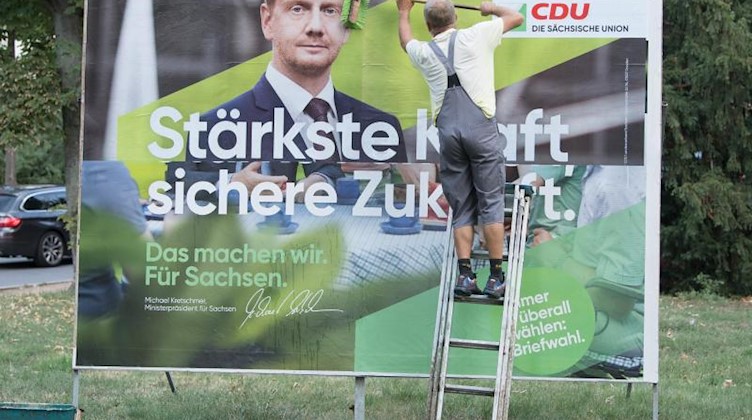 Ein Plakatkleber leimt ein Wahlplakat mit Michael Kretschmer (CDU), Ministerpräsident von Sachsen, ein. Foto: Sebastian Kahnert