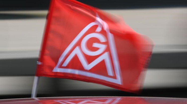 Eine rote IG-Metall-Flagge spiegelt sich in einem Fahrzeugdach. Foto: Patrick Seeger/Archivbild