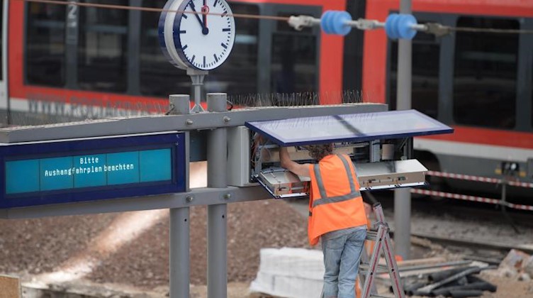 Ein Mann arbeitet im Hauptbahnhof Dresden von einer Leiter aus an einer Anzeigetafel. Foto: Sebastian Kahnert/Archivbild