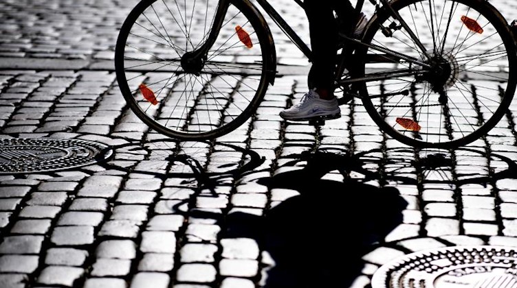 Eine Radfahrerin fährt über Kopfsteinpflaster und wirft einen Schatten. Foto: Guido Kirchner/Archivbild