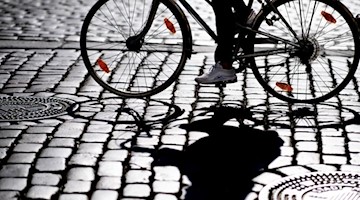 Eine Radfahrerin fährt über Kopfsteinpflaster und wirft einen Schatten. Foto: Guido Kirchner/Archivbild