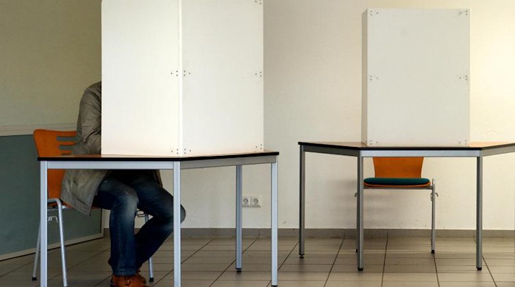 Ein Mann sitzt in einer Wahlkabine. Foto: Peter Endig/Archiv