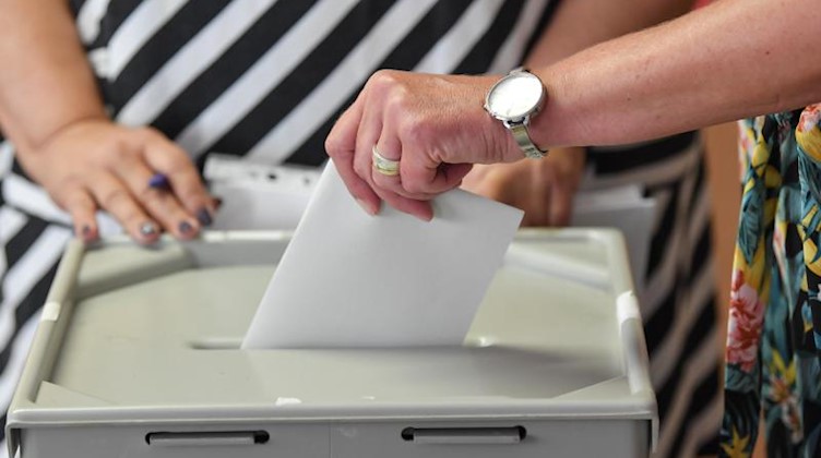 Eine Frau steckt ihren Stimmzettel in eine Wahlurne in einem Wahllokal. Foto: Patrick Pleul
