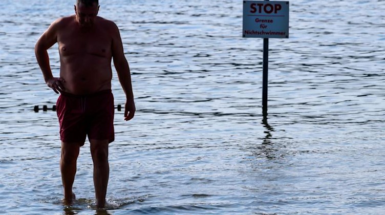 Ein Mann steht dank eines sehr niedrigen Pegelstandes nur knöcheltief im Wasser. Foto: Jens Büttner/Archivbild