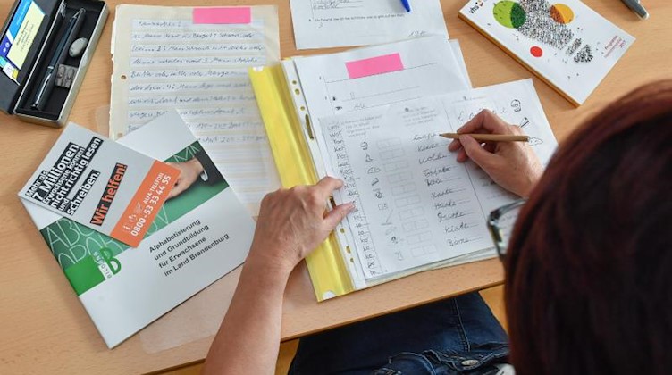 Eine Lehrerin vom Grundbildungszentrum kontrolliert Übungsblätter für Analphabeten. Foto: Patrick Pleul/Archivbild