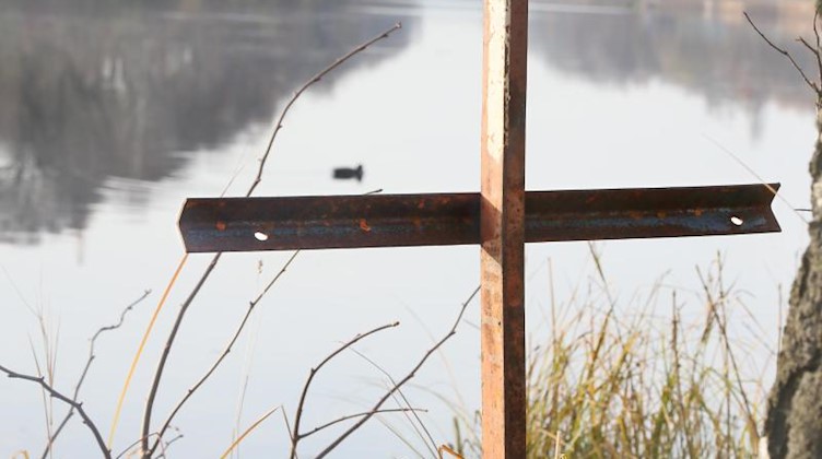 Ein zusammengeschweißtes Metallkreuz steht an einem Gewässer. Foto: Stephanie Pilick/Archivbild
