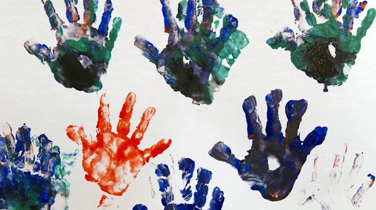 Bunte Handabdrücke eines Dreijährigen sind auf einem weißem Blatt Papier zu sehen. Foto: Peter Kneffel/Archivbild