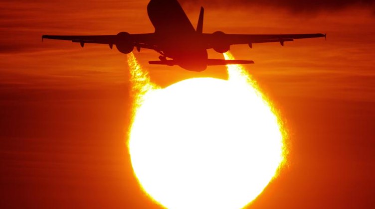 Ein Flugzeug startet vor der untergehenden Sonne. Foto: Julian Stratenschulte/Archiv