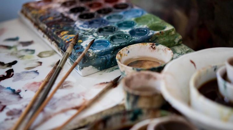 Farben und Pinsel liegen in einer Werkstatt in Meißen. Foto: Monika Skolimowska/Archivbild