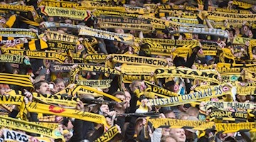 Die Fans von Dynamo Dresden halten ihre Fanschals in die Höhe. Foto: Sebastian Kahnert/Archivbild