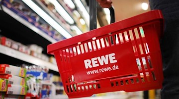 Ein Kunde geht in einem Rewe-Supermarkt mit einem Einkaufskorb am Kühlregal entlang. Foto: Oliver Berg/Archivbild