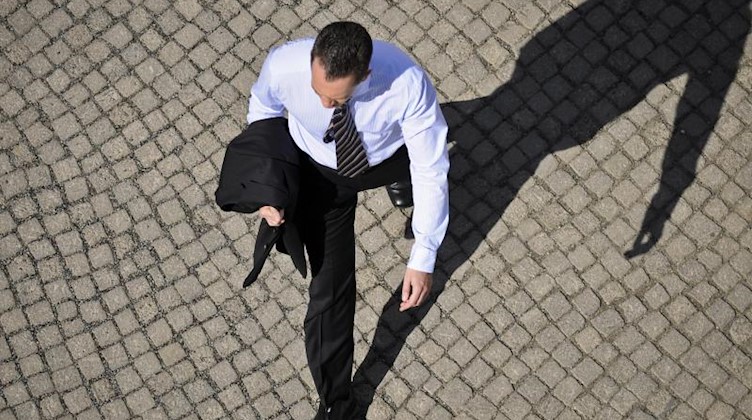 Ein Mann im Anzug wirft einen Schatten auf das Kopfsteinpflaster. Foto: Ole Spata/Archivbild