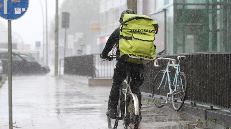 Bei starkem Regen fährt ein Fahrradkurier am Nachmittag auf einem Radweg. Foto: Bodo Marks/dpa