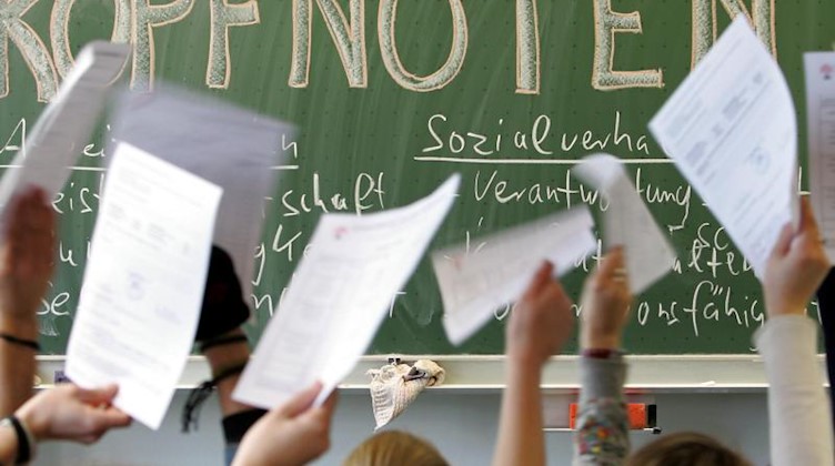 Schüler halten vor der Tafel mit der Aufschrift "Kopfnoten" ihre Zeugnisse nach oben. Foto: Friso Gentsch/dpa