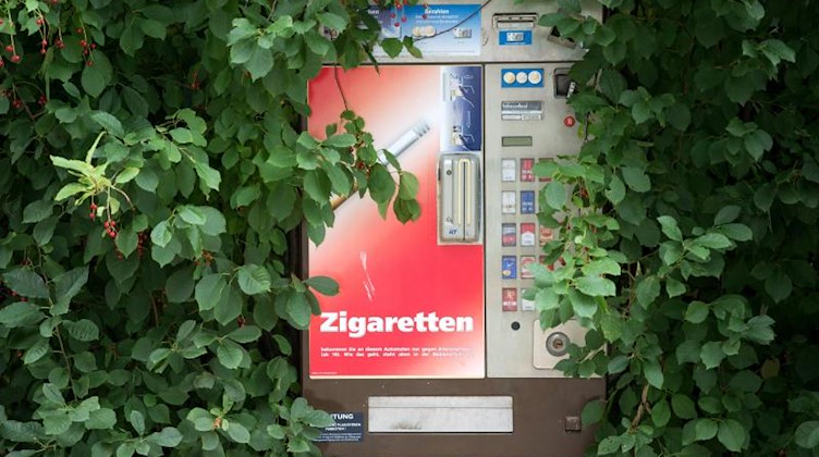 Grünes Blattwerk umrahmt einen Zigarettenautomaten. Foto: Arno Burgi/zb/dpa