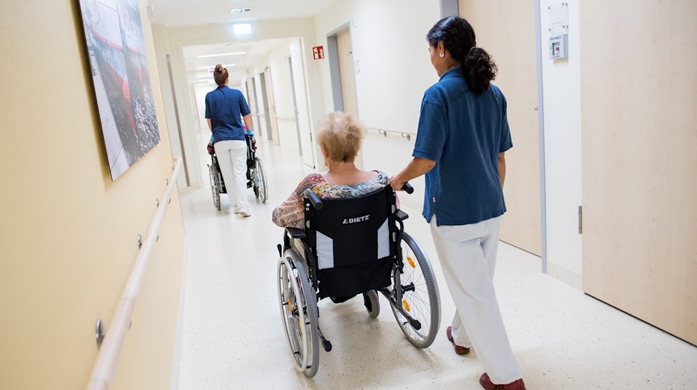 Zwei Pflegerinnen schieben in einem Klinikum Patienten mit Rollstühlen durch einen Flur. / Foto: Daniel Bockwoldt/dpa