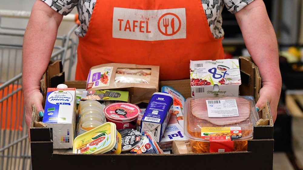 Eine Helferin der Blankenhainer Tafel präsentiert die Kiste mit Lebensmitteln für einen Kunden. / Foto: Martin Schutt/dpa-Zentralbild/dpa