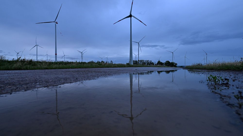 Windräder spiegeln sich in der Morgendämmerung auf in einer Pfütze am Windpark bei Westhausen. / Foto: Martin Schutt/dpa/Archivbild