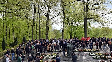 Teilnehmende stehen während einer Kranzniederlegung am Gedenkplatz. / Foto: Martin Schutt/dpa