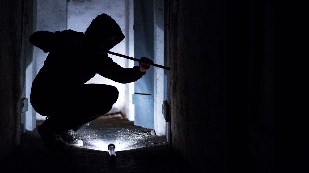 Ein Mann hebelt mit einem Brecheisen eine Tür im Keller eines Wohnhauses auf. / Foto: Silas Stein/dpa