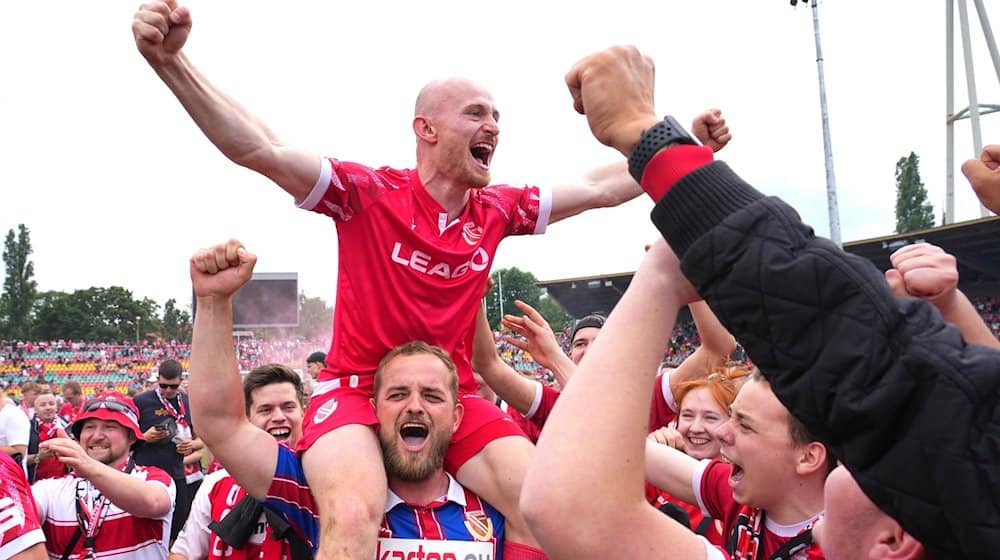 Maximilian Krauß von Cottbus und seine Mitspieler bejubeln nach Schlusspfiff und Platzsturm den Aufstieg mit den Fans. / Foto: Soeren Stache/dpa