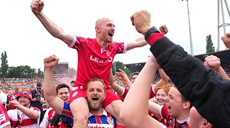 Maximilian Krauß von Cottbus und seine Mitspieler bejubeln nach Schlusspfiff und Platzsturm den Aufstieg mit den Fans. / Foto: Soeren Stache/dpa