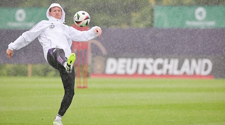 Deutschlands Trainer Julian Nagelsmann spielt einen Ball zu Beginn des Trainings im strömenden Regen. / Foto: Christian Charisius/dpa