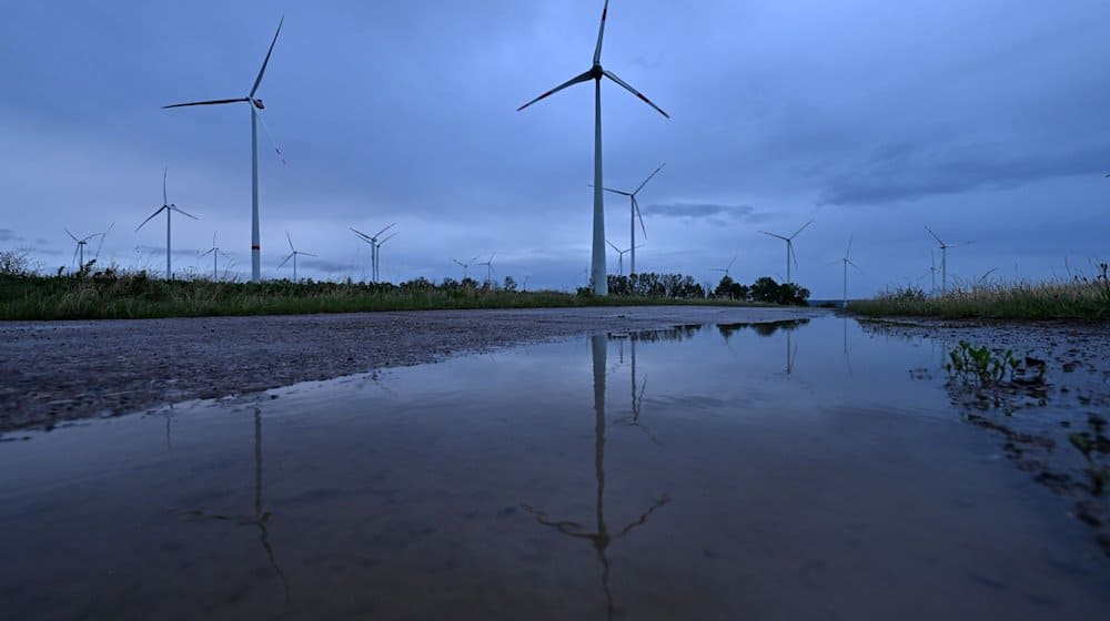 Windräder spiegeln sich in der Morgendämmerung auf in einer Pfütze an einem Windpark. / Foto: Martin Schutt/dpa/Symbolbild