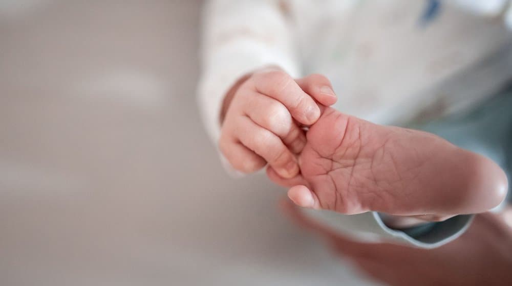 Ein Baby greift mit den Fingern nach seinem Fuß. / Foto: Fabian Strauch/dpa/Symbolbild