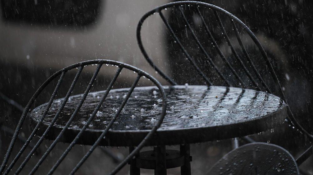 Hagel und Regen prasseln auf einen Tisch vor einem Café. / Foto: Britta Pedersen/dpa