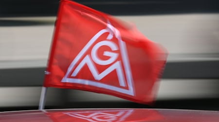 Eine rote IG-Metall-Flagge spiegelt sich in einem Fahrzeugdach. / Foto: Patrick Seeger/dpa/Symbolbild