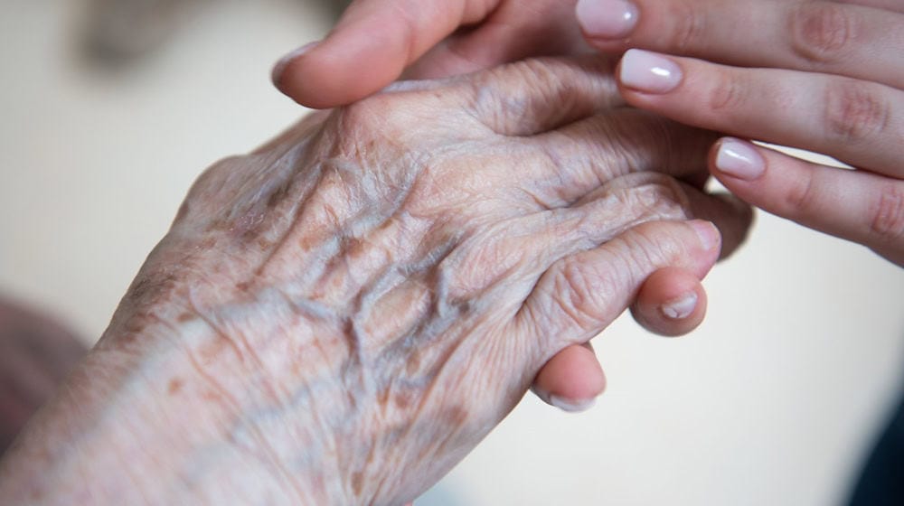 Eine Pflegerin hält die Hand einer Bewohnerin im Seniorenzentrum Sankt Elisabeth. / Foto: Christophe Gateau/dpa/Archivbild