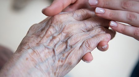 Eine Pflegerin hält die Hand einer Bewohnerin im Seniorenzentrum Sankt Elisabeth. / Foto: Christophe Gateau/dpa/Archivbild