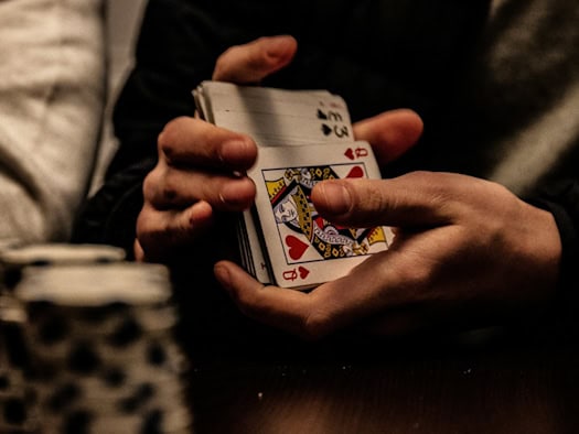 Hände halten ein Kartendeck mit der Dame und dem König Herz während des Mischens an einem Spieltisch