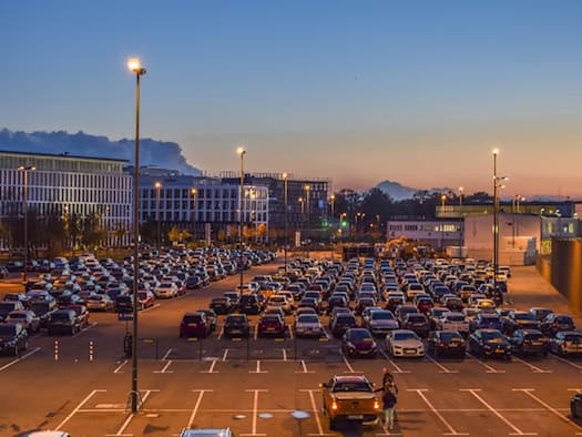Großer Parkplatz mit zahlreichen Gebrauchtwagen bei Abenddämmerung, im Hintergrund moderne Bürogebäude und Gewerbeimmobilien."