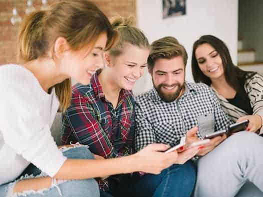 Gruppe junger Erwachsener schaut gemeinsam auf Smartphones