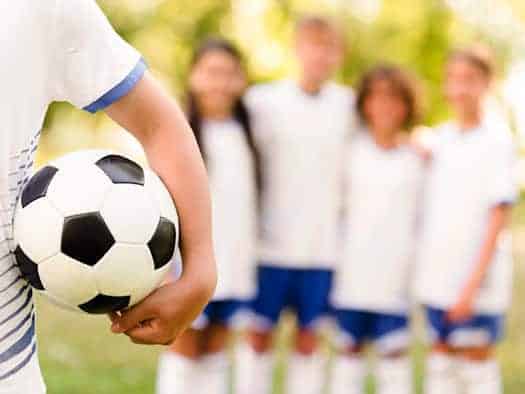 Fußballspieler mit Ball im Vordergrund, im Hintergrund unscharf eine Mannschaft in weißen Trikots
