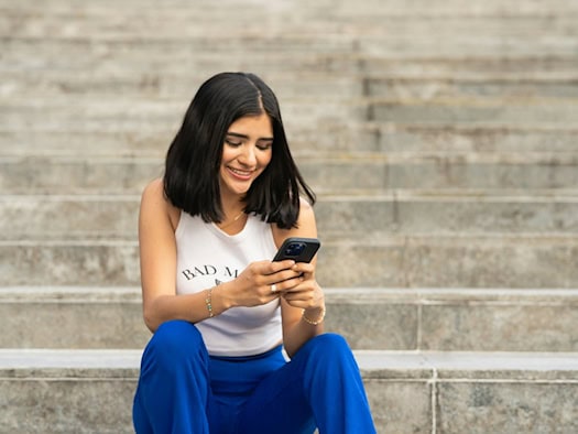 Junge Frau nutzt ein Smartphone auf einer Treppe im Freien – symbolisiert mobile Nutzung und digitale Unterhaltung.