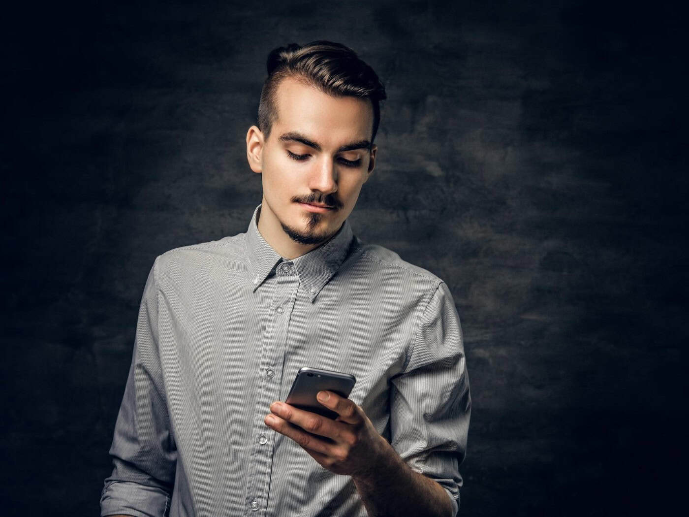 Mann mit Smartphone vor dunklem Hintergrund