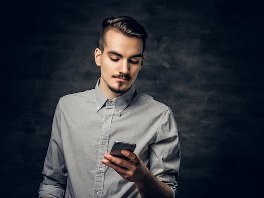 Mann mit Smartphone vor dunklem Hintergrund