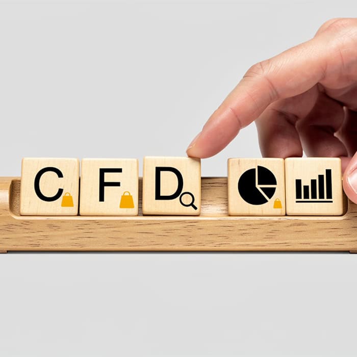 Hand legt Holzblock mit dem Buchstaben "D" zu den Buchstaben "C", "F" und Symbolen für Handel und Analyse, die CFD (Contract for Difference) darstellen.