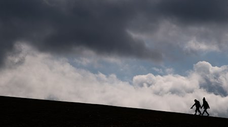 Zwei Kinder laufen auf einen Hügel am Kronsberg, während dunkle Wolken am Horizont vorüberziehen. / Foto: Julian Stratenschulte/dpa