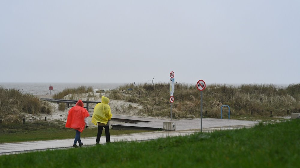 Zwei Tagesgäste laufen bei nassem Wetter in Regenjacken an der Starndpromenade entlang. / Foto: Lars Penning/dpa