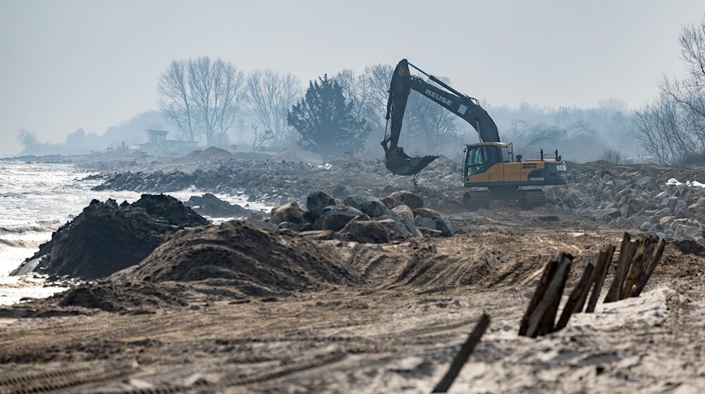 Mit einem Bagger werden große Steine am Strand am Hafen von Damp verladen. / Foto: Axel Heimken/dpa