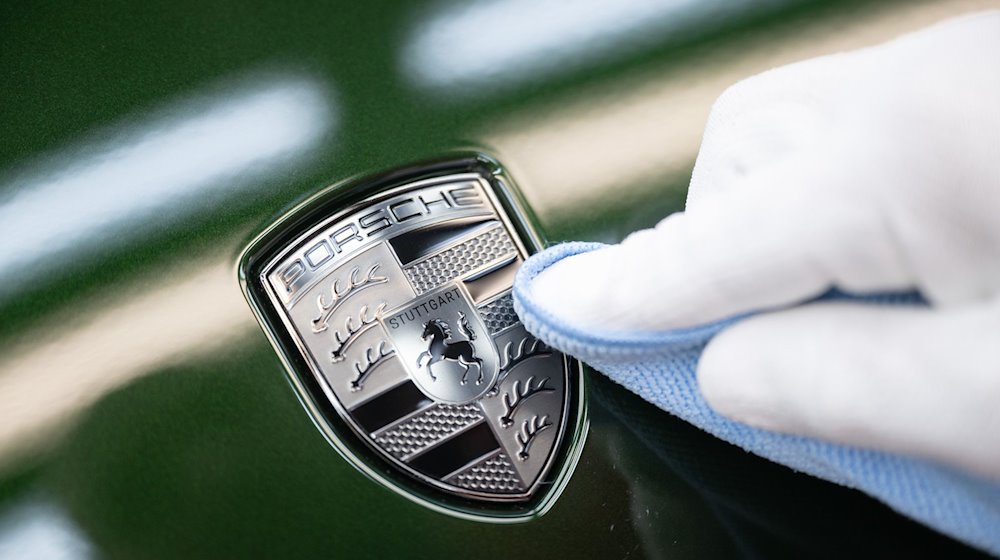 Ein Mitarbeiter der Porsche AG reinigt im Stammwerk in Zuffenhausen das Porsche-Wappen auf der Motorhaube eines vollelektrischen Porsche Taycan, nachdem er es angebracht hat. / Foto: Marijan Murat/dpa