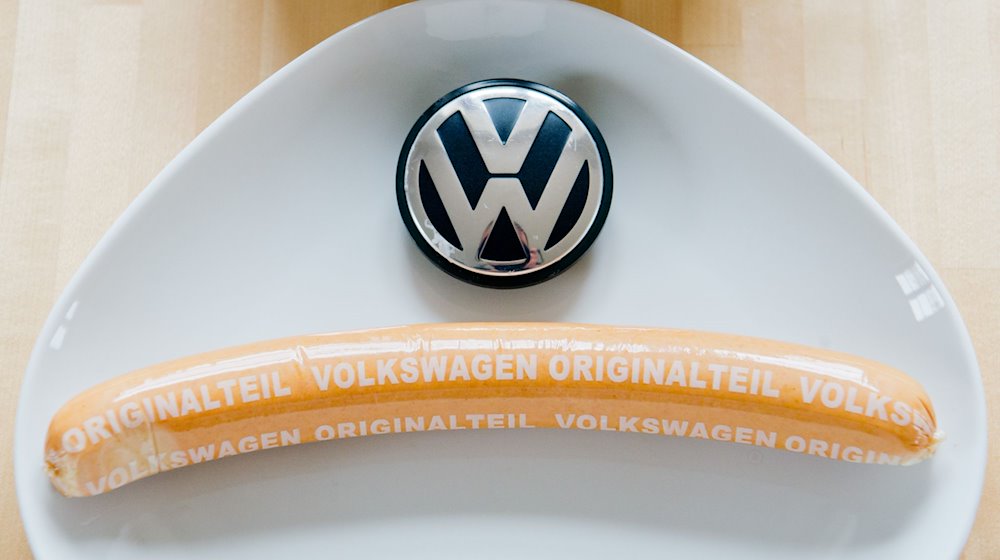 Eine Currywurst mit Aufschrift «Volkswagen Originalteil» und ein VW-Logo liegen auf einem Teller. / Foto: Julian Stratenschulte/dpa/Symbolbild