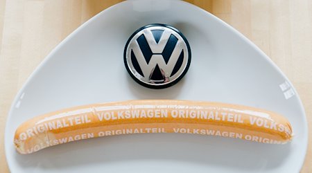 Eine Currywurst mit Aufschrift «Volkswagen Originalteil» und ein VW-Logo liegen auf einem Teller. / Foto: Julian Stratenschulte/dpa/Symbolbild