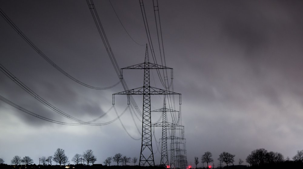 Dunkle Wolken ziehen über eine Hochspannungsleitung hinweg. / Foto: Julian Stratenschulte/dpa